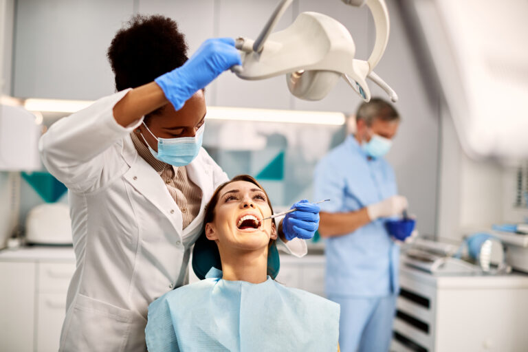 Black female dentist examining teeth of young woman at dental clinic.